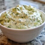 Close-up of a creamy, chunky homemade pickle dip mixed with fresh dill, served in a white bowl.