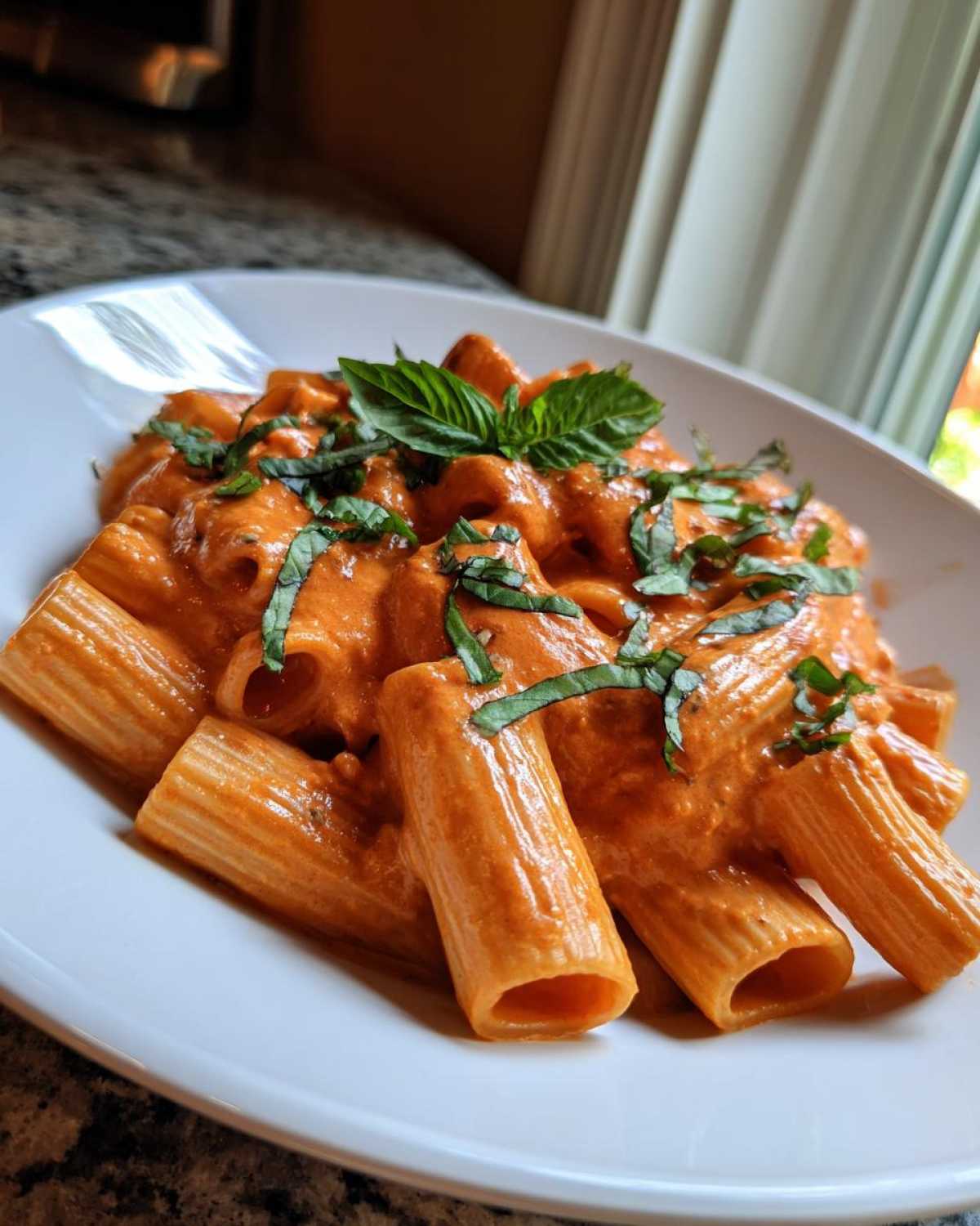 Close-up of rigatoni pasta coated in rich, creamy pink sauce pasta, garnished with fresh basil leaves.