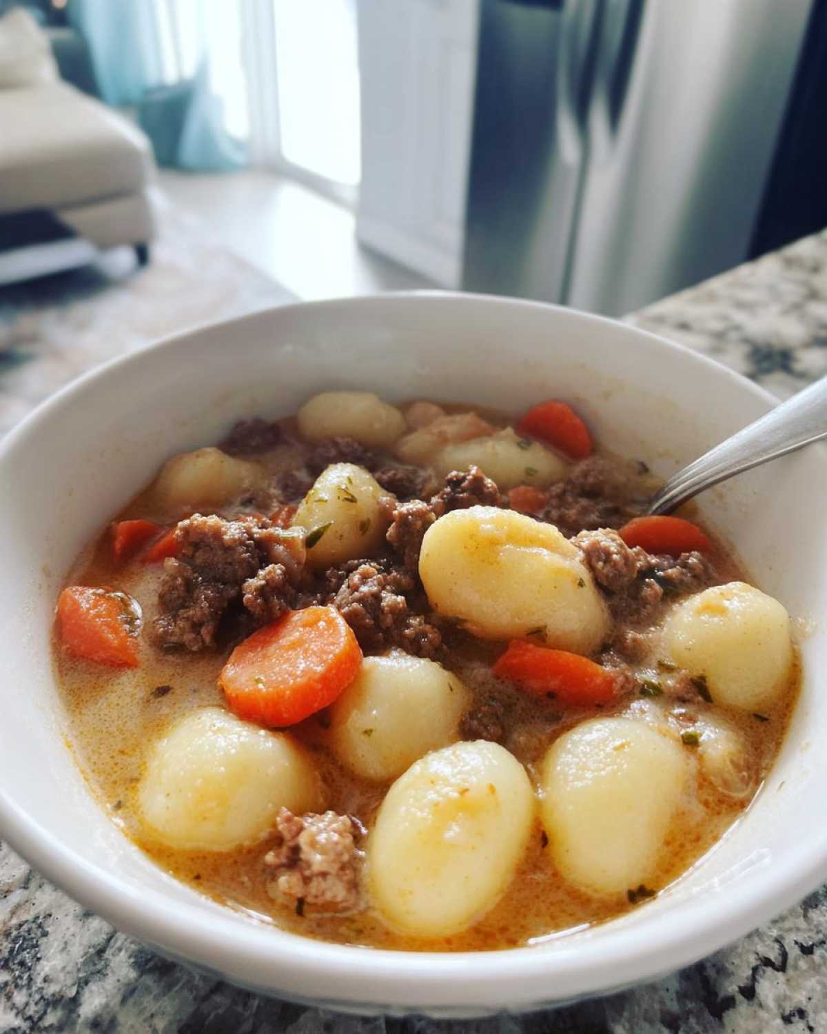Close-up of a bowl of creamy sausage gnocchi soup with visible carrots and ground sausage.