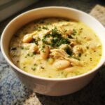A close-up of creamy white chicken chili recipe, featuring shredded chicken, white beans, and fresh parsley garnish.