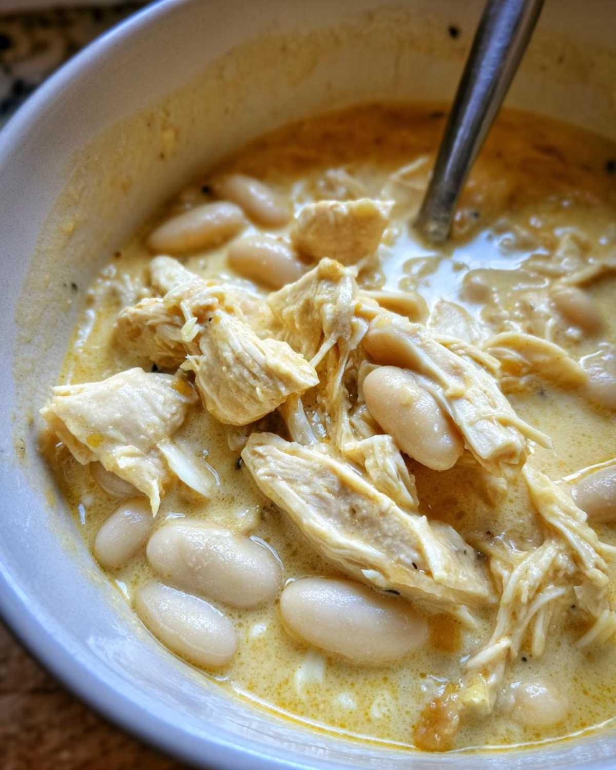 Close-up of creamy white chicken chili recipe featuring shredded chicken and white beans in a yellow broth.