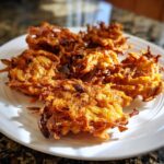 Close-up of several crispy, golden brown Amish Onion Fritters piled on a white plate.