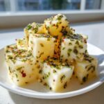Close-up of cubed marinated cheese coated in oil, green herbs, and red pepper flakes.