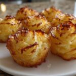 Close-up of several golden brown duchess potatoes piped into beautiful rose shapes on a white plate.