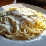 Close-up of fettuccine pasta generously coated in creamy Olive Garden Alfredo Sauce and topped with black pepper.