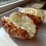A close-up of a perfectly cooked air fryer baked potato, split open to show the fluffy white interior.