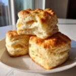 Three tall, square buttermilk biscuits stacked on a white plate, showing flaky layers.