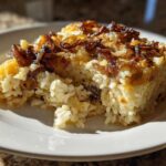 A square portion of baked french onion butter rice topped with crispy, caramelized onions on a white plate.