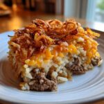 A square serving of french onion ground beef and rice casserole topped with melted cheese and crispy fried onions.