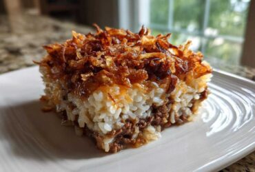 A square slice of french onion ground beef and rice casserole with crispy fried onions on top.