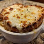 Close-up of a serving of french onion soup with a thick layer of melted, browned cheese over toasted bread.