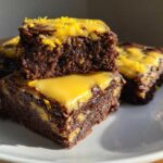 Close-up of stacked, fudgy lemon brownies topped with bright yellow lemon glaze and zest.