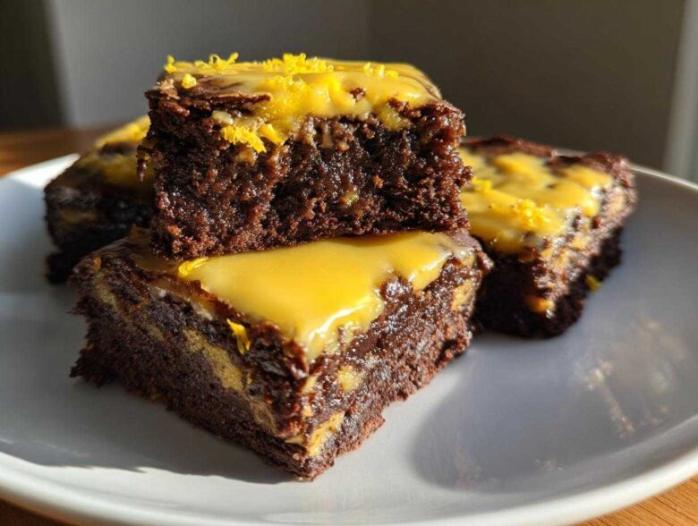 Close-up of stacked, fudgy lemon brownies topped with bright yellow lemon glaze and zest.