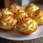 Close-up of several golden brown duchess potatoes piped into beautiful rosette shapes on a white plate.