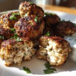 Close-up of golden brown greek chicken meatballs, one cut open, served with a dollop of tzatziki sauce.