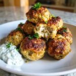 A stack of perfectly browned greek chicken meatballs served with a dollop of creamy tzatziki sauce.