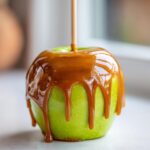 Close-up of a bright green apple coated in thick, dripping caramel sauce, ready to eat as a caramel apples treat.