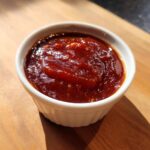 Close-up of rich, thick homemade bbq sauce served in a small white ramekin on a wooden surface.