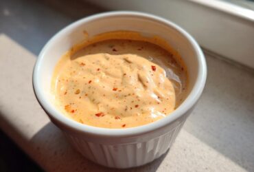 Close-up of creamy, orange-hued big mac sauce speckled with red pepper flakes in a small white bowl.
