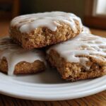 Close-up of three soft, square iced oatmeal cookies stacked on a white plate, drizzled with white glaze.