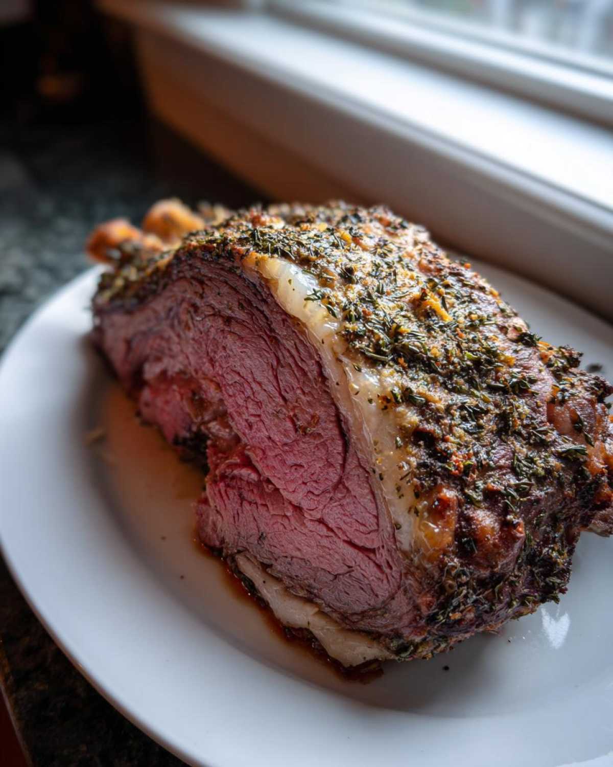 Close-up of a juicy, medium-rare rib roast slice with a thick herb crust resting on a white plate.