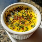 Close-up of melted, bright yellow cowboy butter dipping sauce topped with green herbs and red pepper flakes.