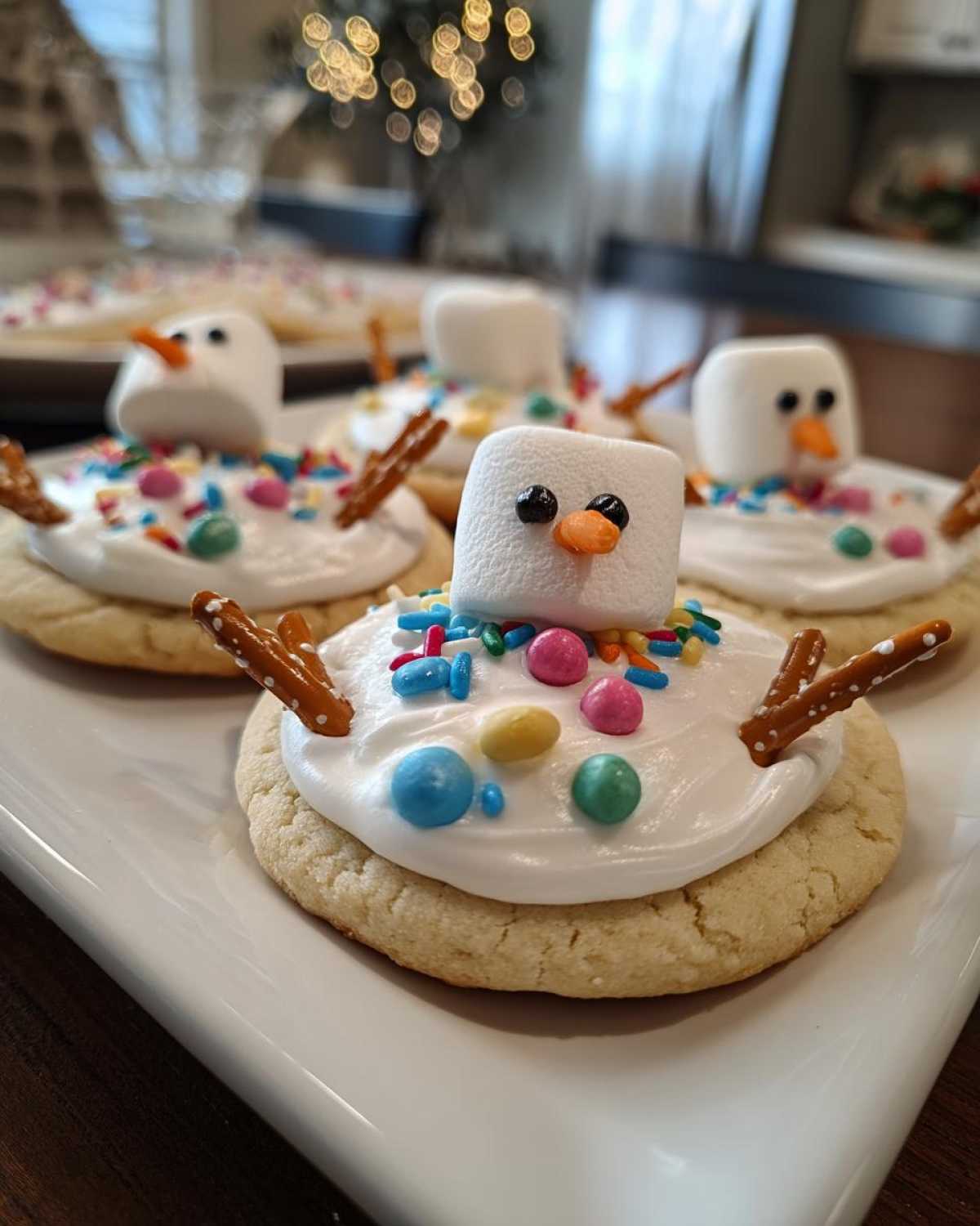 Close-up of several melted snowman cookies featuring a marshmallow head, pretzel arms, and colorful sprinkles.