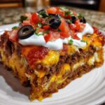 A thick, layered slice of Mexican pizza topped with melted cheese, sour cream, diced tomatoes, and black olives.