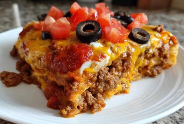 A close-up slice of 5-layer Mexican pizza topped with melted cheese, salsa, diced tomatoes, and black olives.