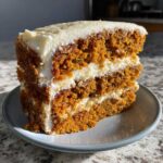 Close-up of a thick slice of moist carrot cake recipe with two layers of cream cheese frosting.