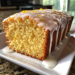 Close-up of a moist slice of lemon loaf cake topped with thick white glaze and bright orange lemon zest.