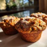 Three golden brown morning glory muffins topped with walnuts and powdered sugar, bathed in sunlight.