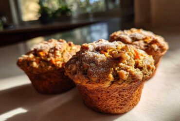 Three golden brown morning glory muffins topped with walnuts and powdered sugar, bathed in sunlight.