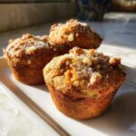 Three golden brown morning glory muffins topped with walnuts and coarse sugar, sitting on a white platter.