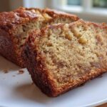 Close-up of a moist slice of vegan banana bread with a dark, caramelized crust, served on a white plate.
