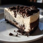 A perfect slice of creamy no-bake Oreo cheesecake with a dark chocolate crust and crushed Oreo topping.