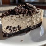 A close-up slice of creamy no-bake Oreo cheesecake with a dark cookie crust and crumbled topping.