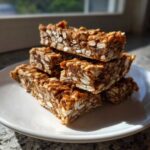 A stack of homemade, chewy, no-bake protein bars made with oats, glistening in natural sunlight.