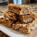 A stack of homemade, chewy no-bake protein bars made with oats, displayed on a rectangular white plate.