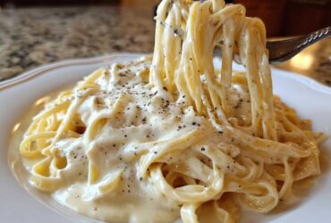 Fork lifting fettuccine noodles coated in rich, creamy Olive Garden Alfredo Sauce and black pepper.