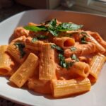 A close-up of rigatoni pasta coated in creamy pink sauce pasta, garnished with fresh basil leaves.