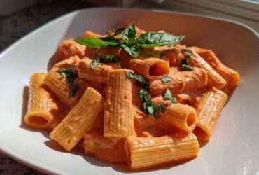 A close-up of rigatoni pasta coated in creamy pink sauce pasta, garnished with fresh basil leaves.