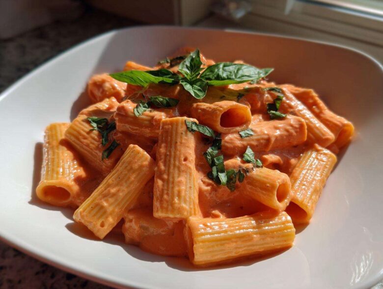 A close-up of rigatoni pasta coated in creamy pink sauce pasta, garnished with fresh basil leaves.