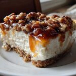 A thick slice of creamy pecan pie dip on a white plate, topped with gooey caramel and chopped pecans.