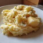 A close-up of fluffy roasted garlic mashed potatoes topped with melted butter and herbs on a white plate.
