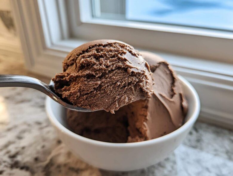 A spoonful of rich, dark chocolate mousse being lifted from a white bowl near a window.