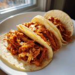 Three soft corn tortillas filled with saucy, shredded chicken filling, ready to eat chicken tacos.