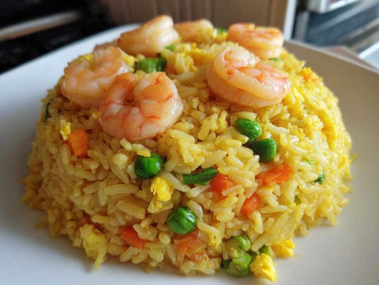 A mound of yellow shrimp fried rice topped with perfectly cooked pink shrimp, peas, and carrots.