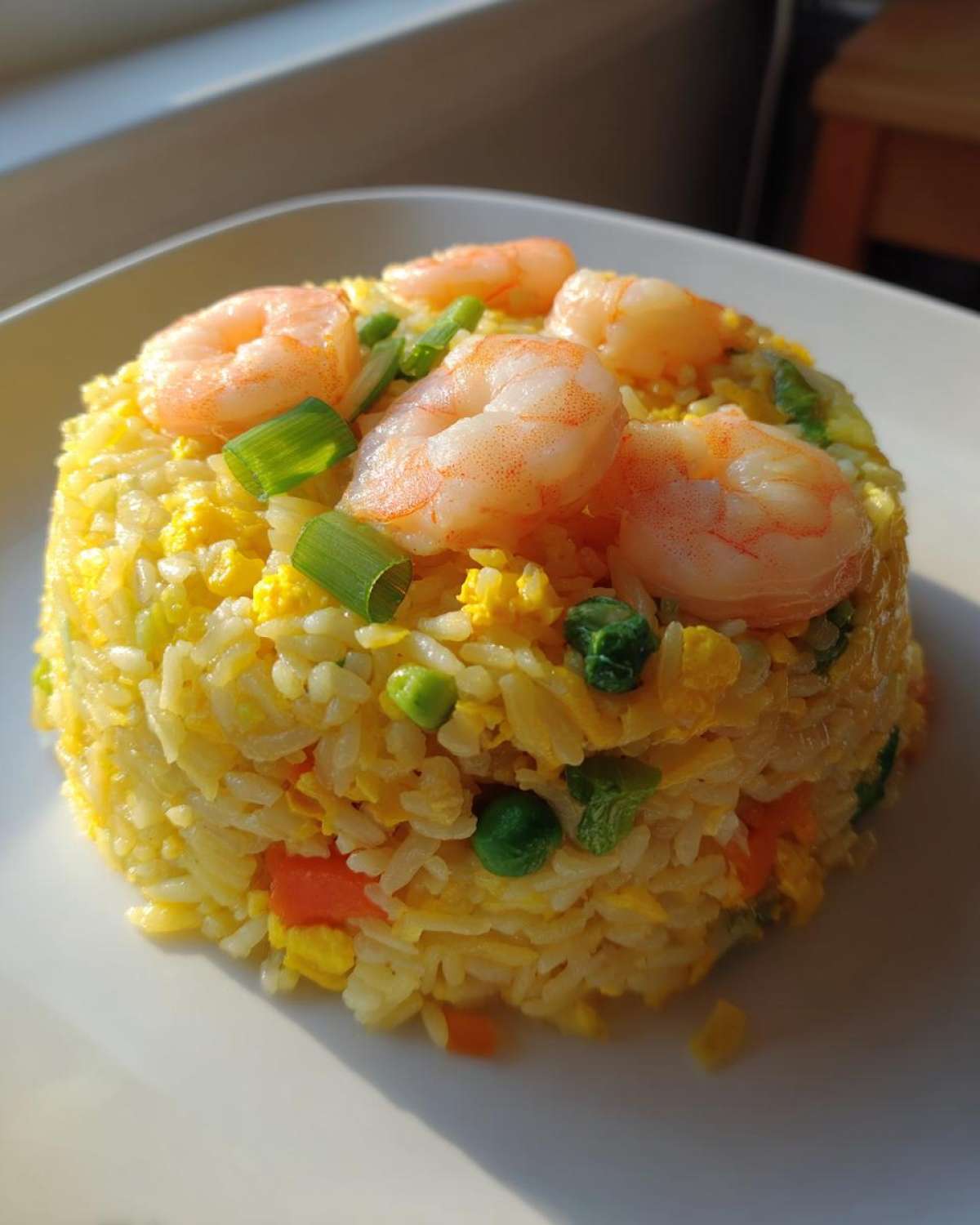 A molded serving of bright yellow shrimp fried rice topped with pink shrimp and green onions.