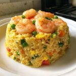 A perfectly molded serving of vibrant shrimp fried rice recipe topped with large cooked shrimp.